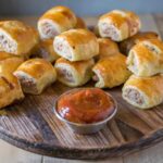 Mini sausage rolls stacked on a board with ketchup