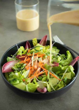 Pouring miso salad dressing over lettuce greens and shredded carrots