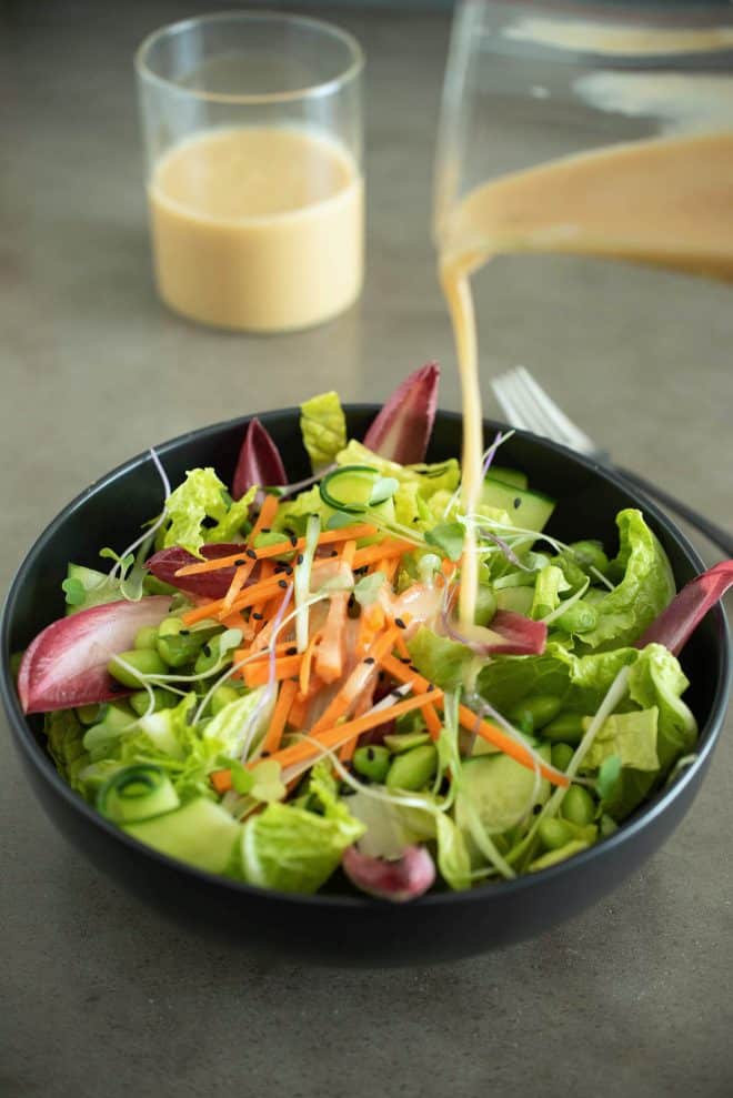 Pouring miso dressing onto a bowl of salad greens and vegetables