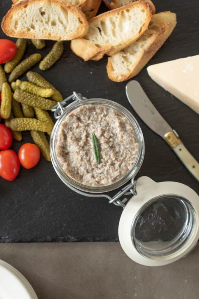 An overhead view of creamy pate with crusty bread, pickles and tomatoes