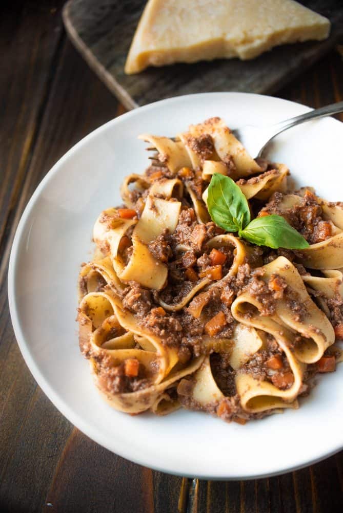 A closeup showing mushroom Bolognese mixed with pappardelle pasta that looks meaty garnished with basil leaves in a white pasta bowl