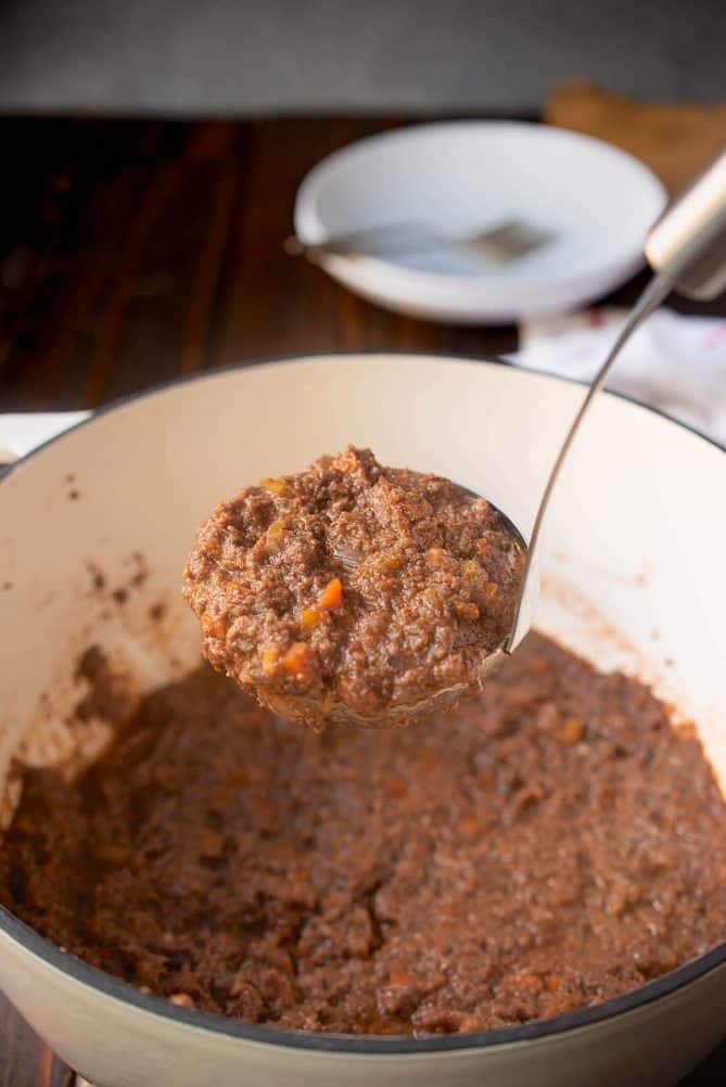 A ladle full of mushroom Bolognese sauce, lifting it out a pan
