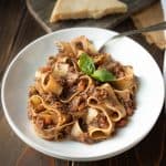 Long, wide pasta noodles curled up in a pasta bowl covered with mushroom Bolognese sauce with some pasta twirled around a fork