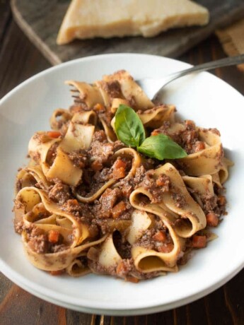 Long, wide pasta noodles curled up in a pasta bowl covered with mushroom Bolognese sauce with some pasta twirled around a fork