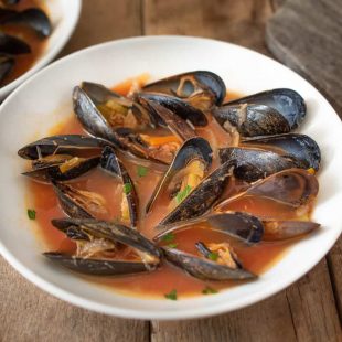 A large bowl of mussels in tomato broth with grilled bread