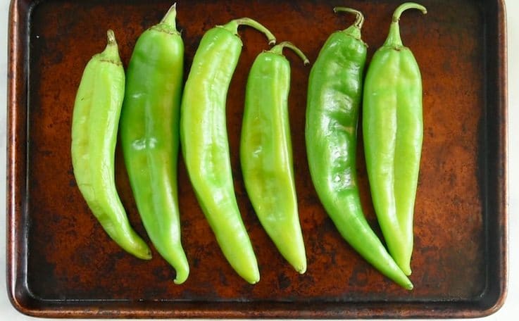 Green hatch chiles are lined up on a baking sheet ready to be broiled