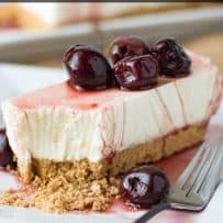 A rectangle piece of cherry lemon cheesecake on a plate with a bite taken out