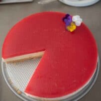 A vibrant red strawberry cheesecake decorated with edible pansy flowers