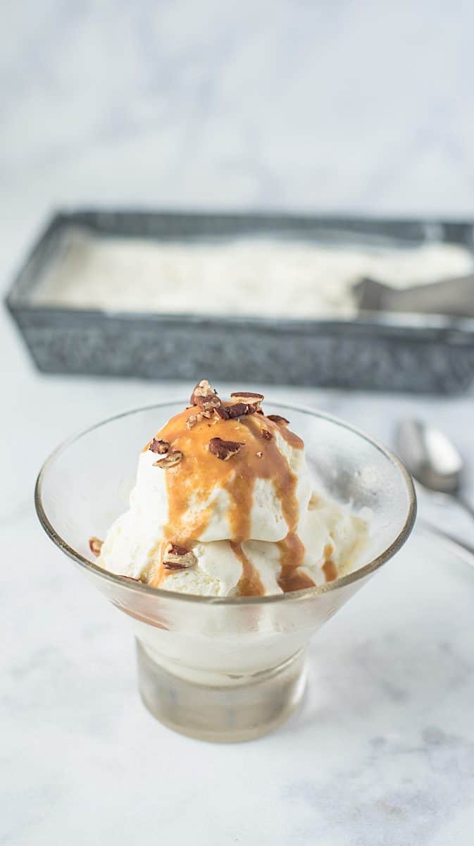 No churn vanilla bean ice cream in a glass bowl topped with caramel and chopped pecans