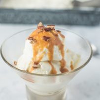 No churn vanilla bean ice cream in a round glass bowl with caramel and pecans