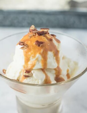 No churn vanilla bean ice cream in a round glass bowl with caramel and pecans