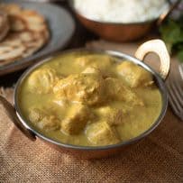 A copper bowl filled with yellow Indian chicken curry