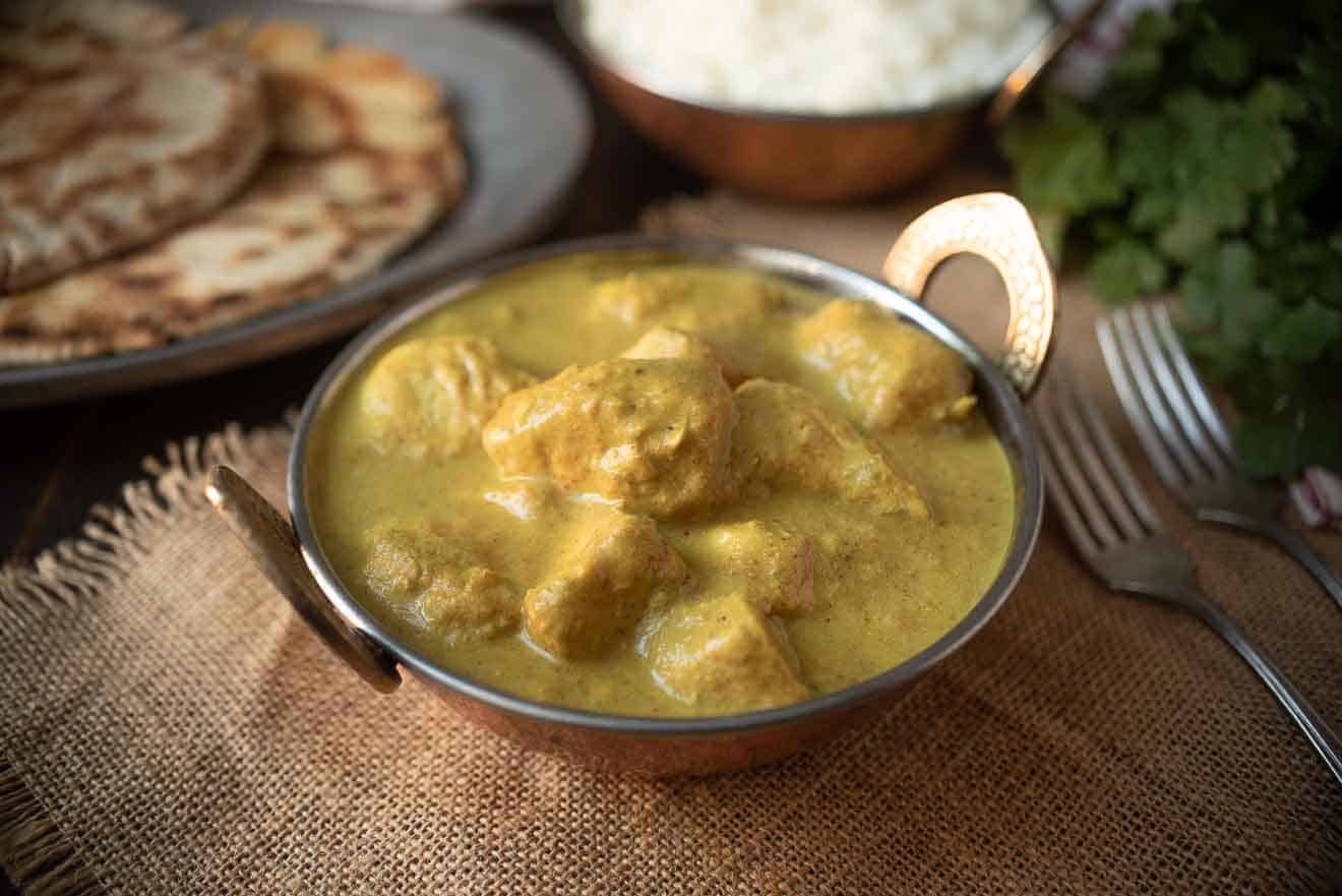 A copper bowl filled with yellow Indian chicken curry