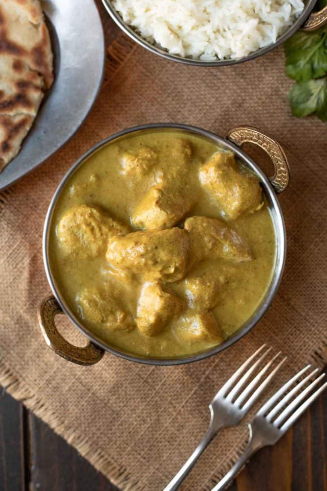 Viewed from overhead, large pieces of chicken in a yellow Indian chicken korma curry sauce