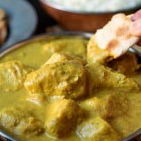 Chicken chunks in a yellow curry with a piece of naan bread