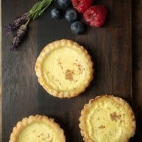 3 egg custard tarts viewed from overhead with fresh lavender flowers, raspberries and blueberries