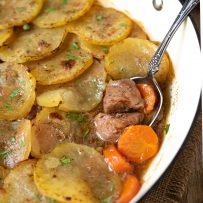 A closeup of tender pieces of lamb and carrot in a pan topped with sliced potatoes