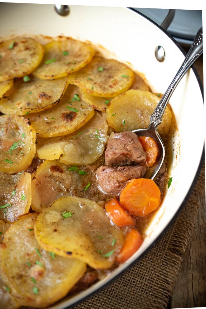 A closeup of tender pieces of lamb and carrot in a pan topped with sliced potatoes