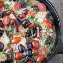 Chicken breasts, olives, cherry tomatoes, herbs and wine cooking in a cast iron skillet