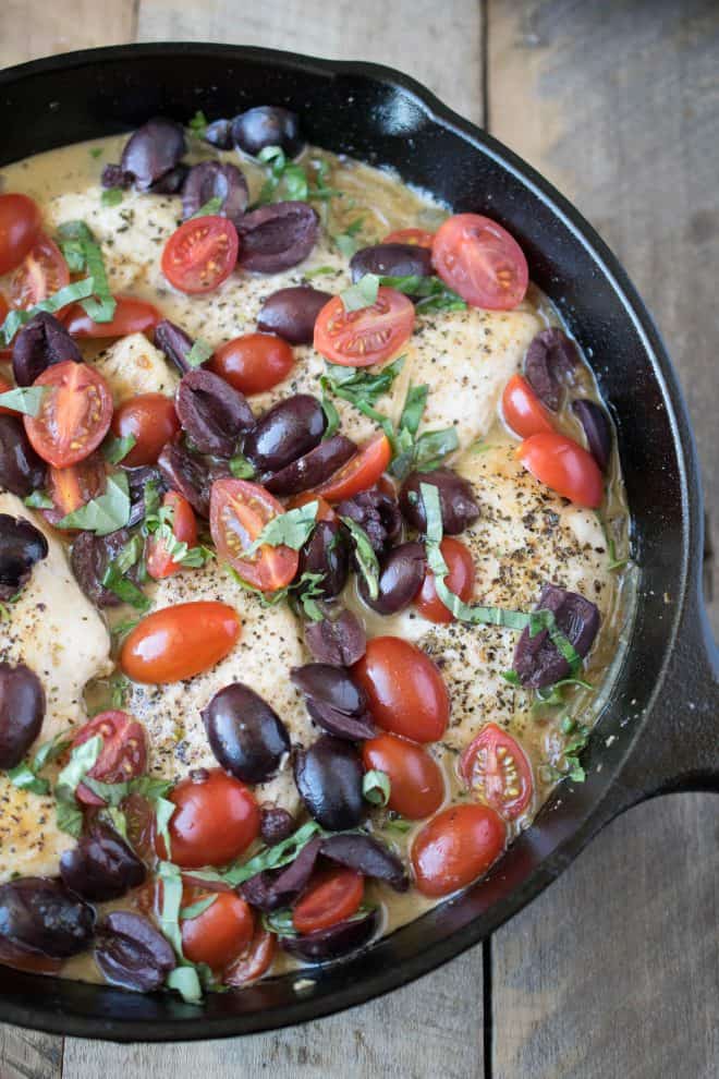 Chicken breasts, olives, cherry tomatoes, herbs and wine cooking in a cast iron skillet