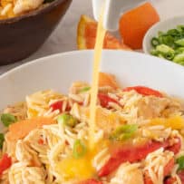 Orange vinaigrette dressing being poured over chicken and orzo salad with vegetables