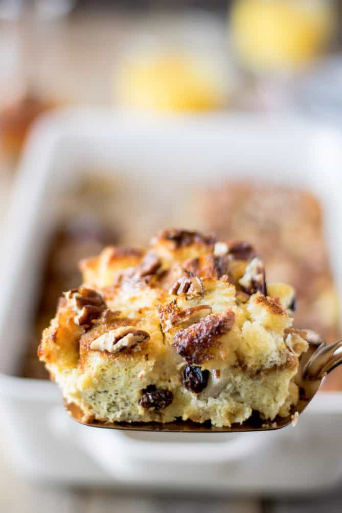 A slice of French toast casserole on a spatula showing the raisins inside and pecans on top