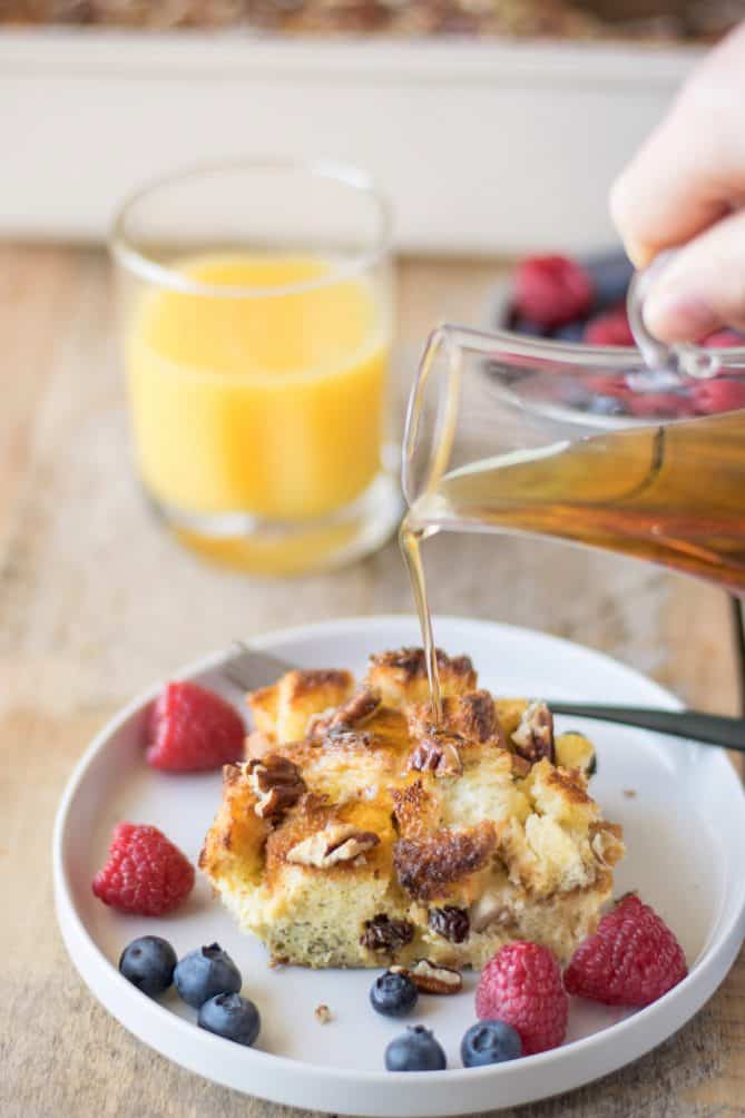Pouring syrup over a piece of French toast casserole with raspberries and blueberries