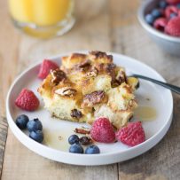 A slice of the French toast casserole on a white plate with blueberries and raspberries