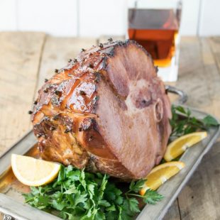 A beautifully glazed ham on a serving tray garnished with orange sliced and parsely