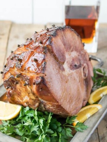 A beautifully glazed ham on a serving tray garnished with orange sliced and parsely