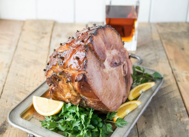 A beautifully glazed ham on a serving tray garnished with orange sliced and parsely