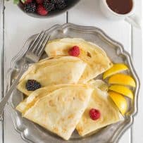 Thin crepe pancakes with lemon wedges fruit and syrup from overhead