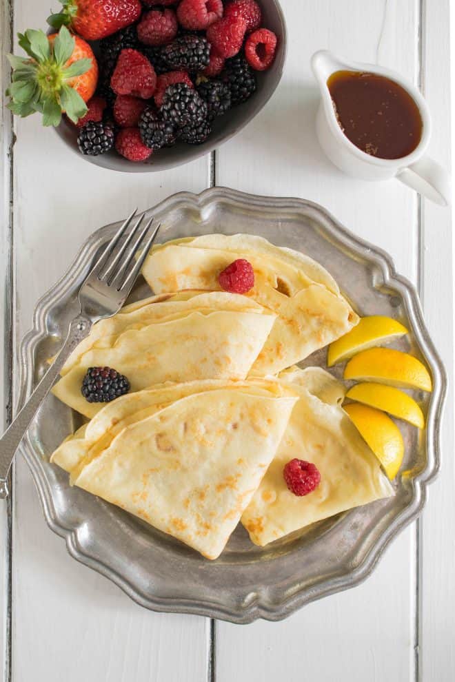 Thin crepe pancakes with lemon wedges fruit and syrup from overhead