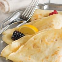 Crepe style pancakes folded on a plate with fruit and lemon