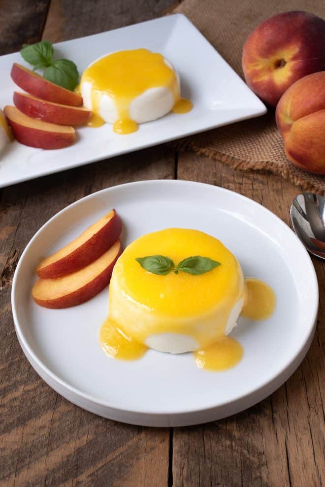 Panna cotta drizzled with peach sauce on a white plate with fresh peach slices