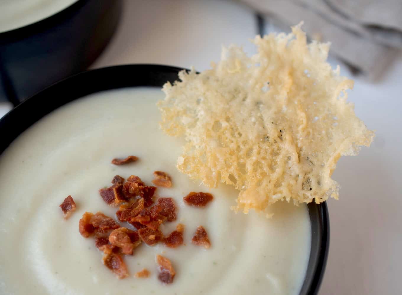 A crispy Parmesan cracker with a bowl of soup