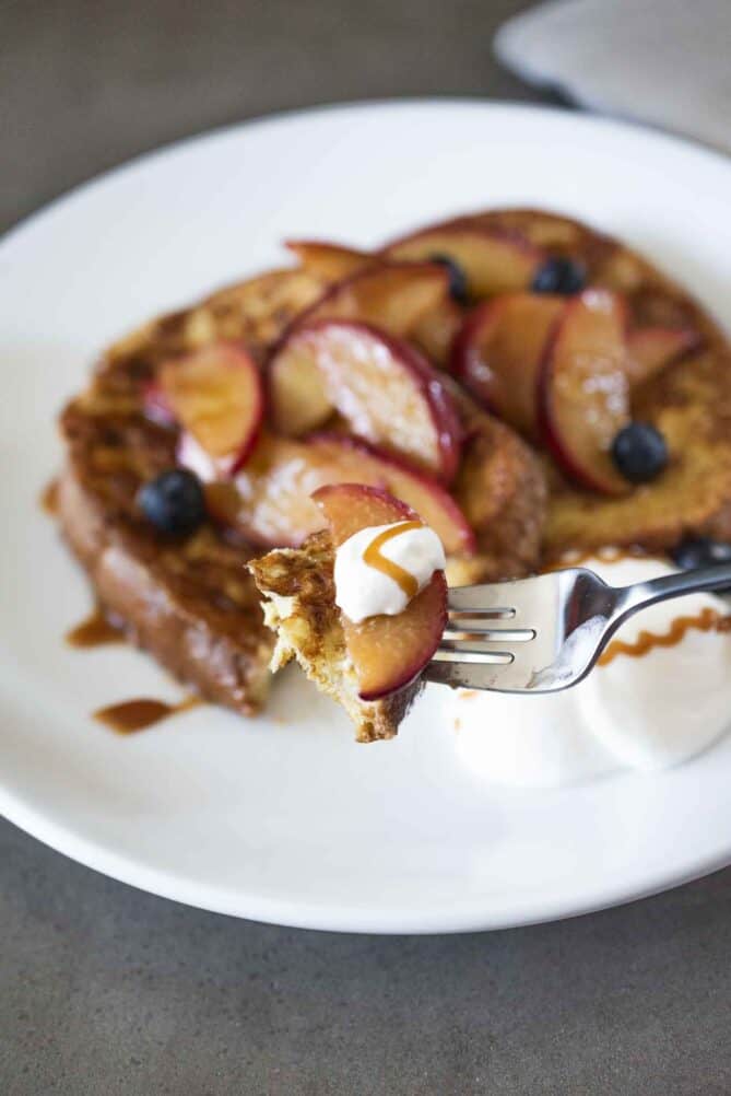 A bite of French toast with peach on a fork