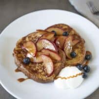 Caramelized peach slices on top of French toast with blueberries and whipped cream