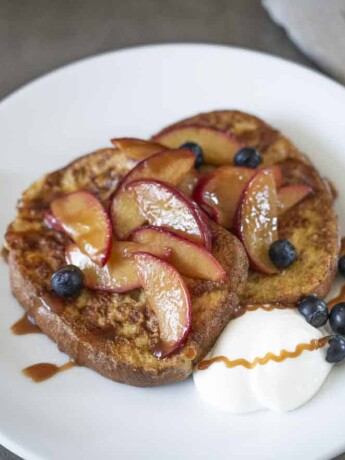 Caramelized peach slices on top of French toast with blueberries and whipped cream