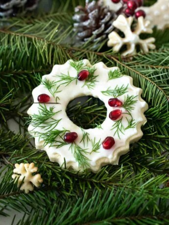 A peppermint cookie decorated with white icing, green leaves and pomegranate seeds