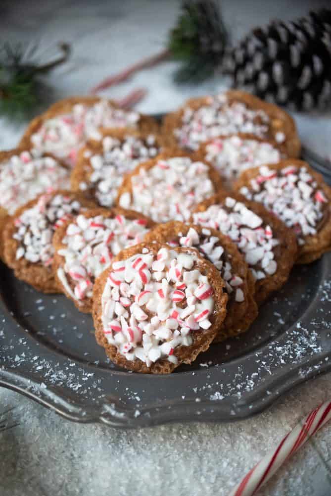 Crushed candy canes on top of lace sandwich cookies displayed on a grey plate