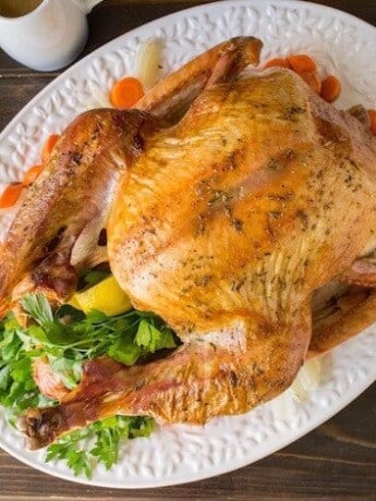 An overhead image of a roast turkey on a white platter with stuffing, mash and cranberry sauce