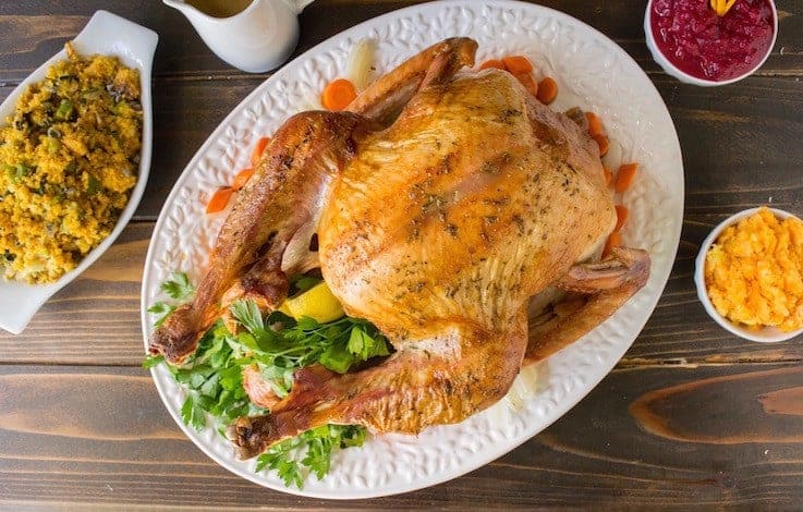 An overhead image of a roast turkey on a white platter with stuffing, mash and cranberry sauce