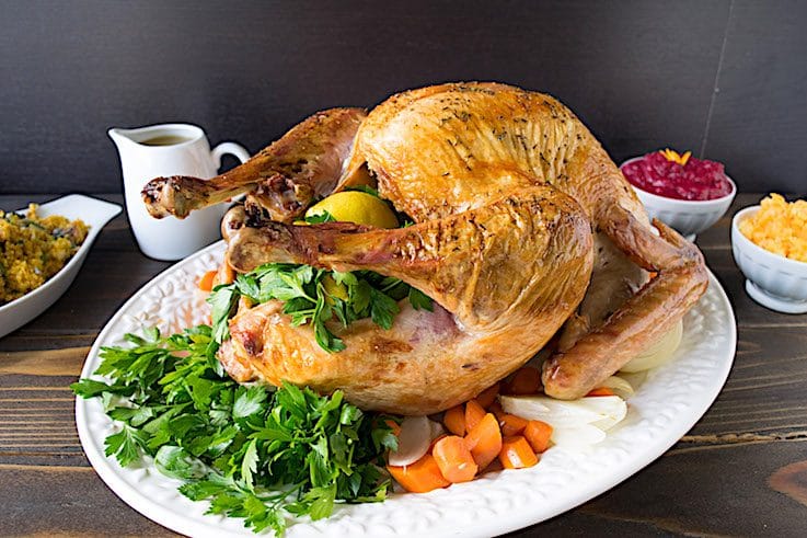 A roast turkey on a white plate garnished with fresh parsley, lemon and carrots