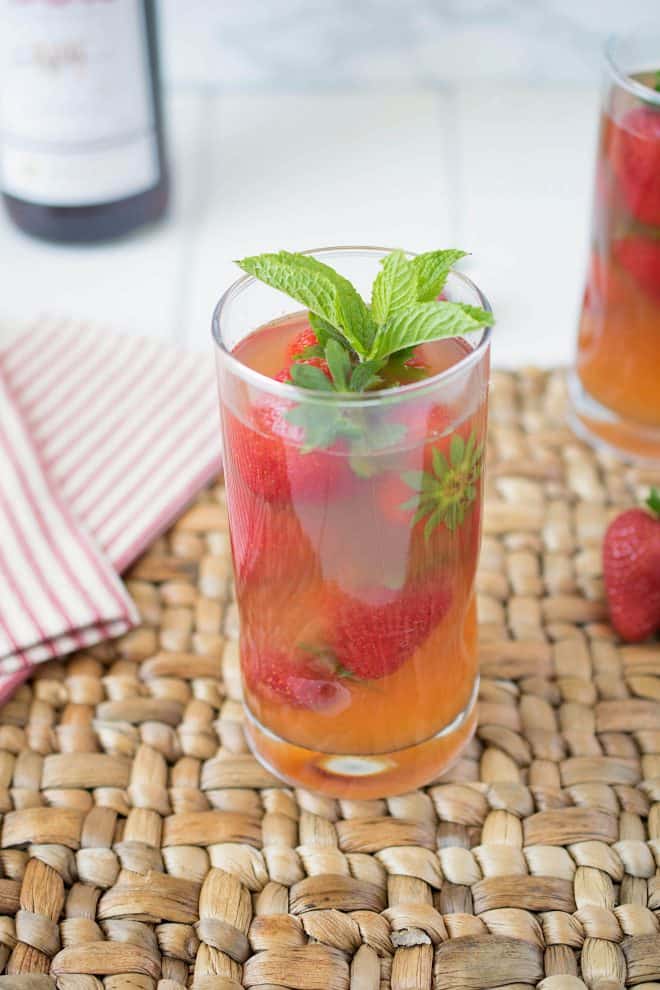 A tall glass of Pimm's strawberry mint cocktail garnished with fresh strawberries and mint