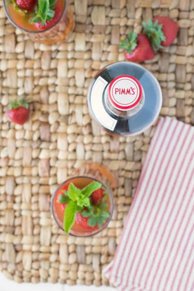 A view from overhead of the Pimm's bottle and drink with fresh strawberries and a striped napkin
