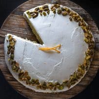 The pistachio cake viewed from overhead with a slice remove and fresh orange garnish