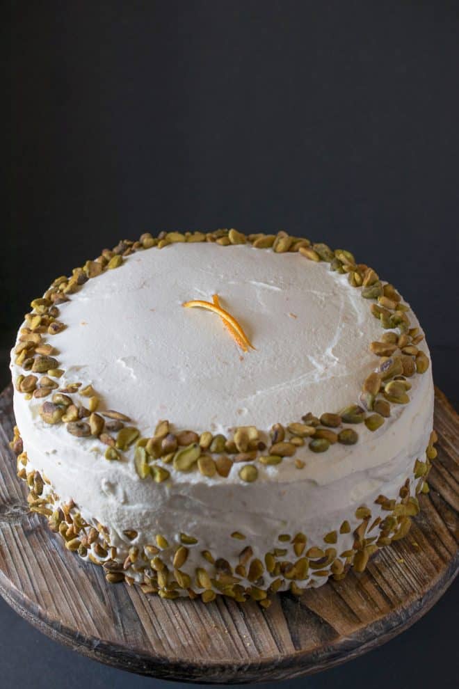 An uncut pistachio cake with orange cream frosting decorated with pistachio pieces