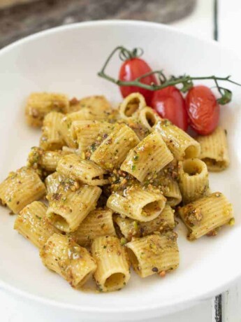 A bowl of pistachio pesto pasta with cherry tomatoes on the vine