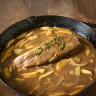 A cast iron skillet with apple and ale gravy and pork tenderloin